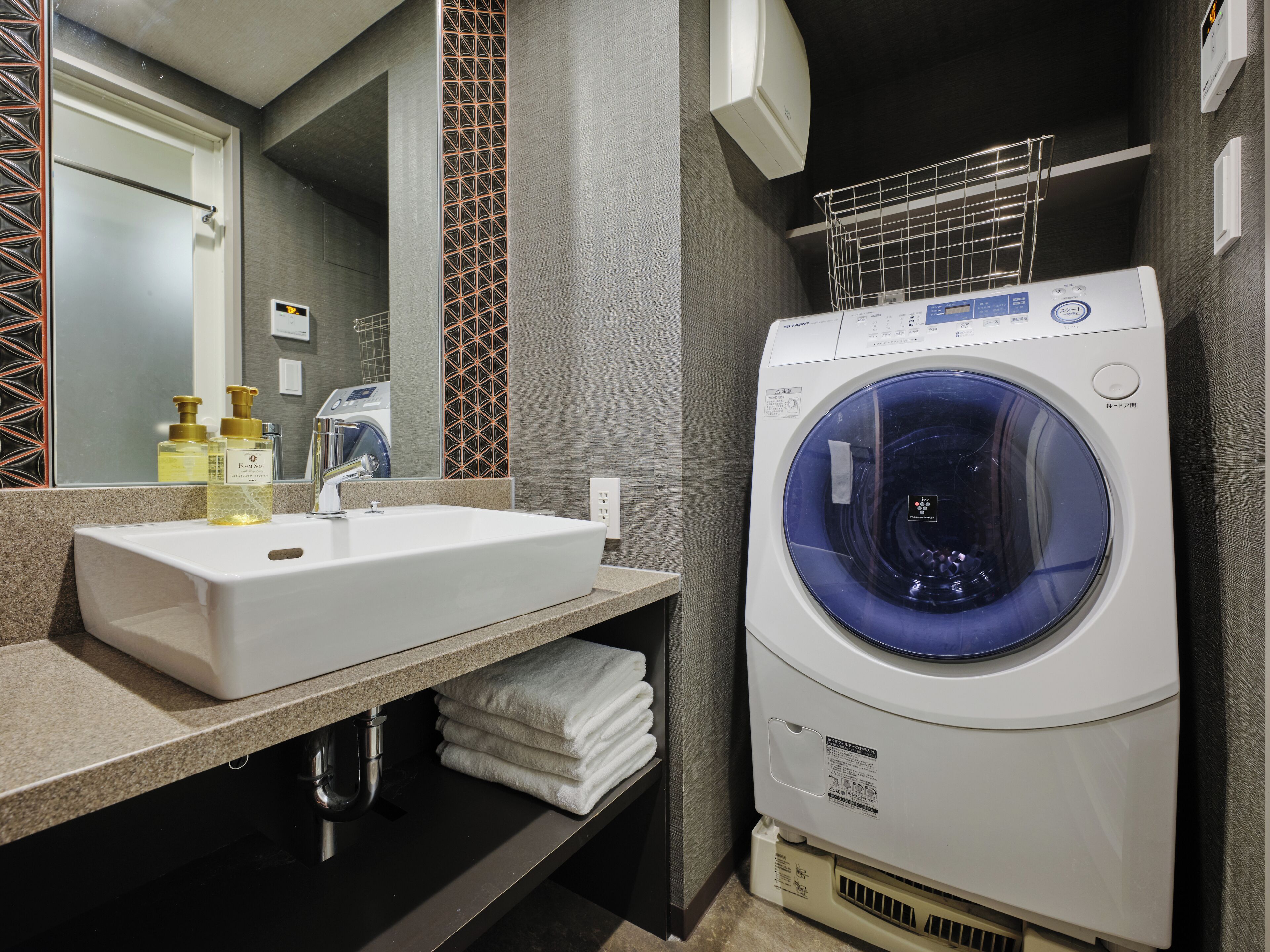 A modern bathroom with a white sink, a built-in washing machine, and a towel rack.