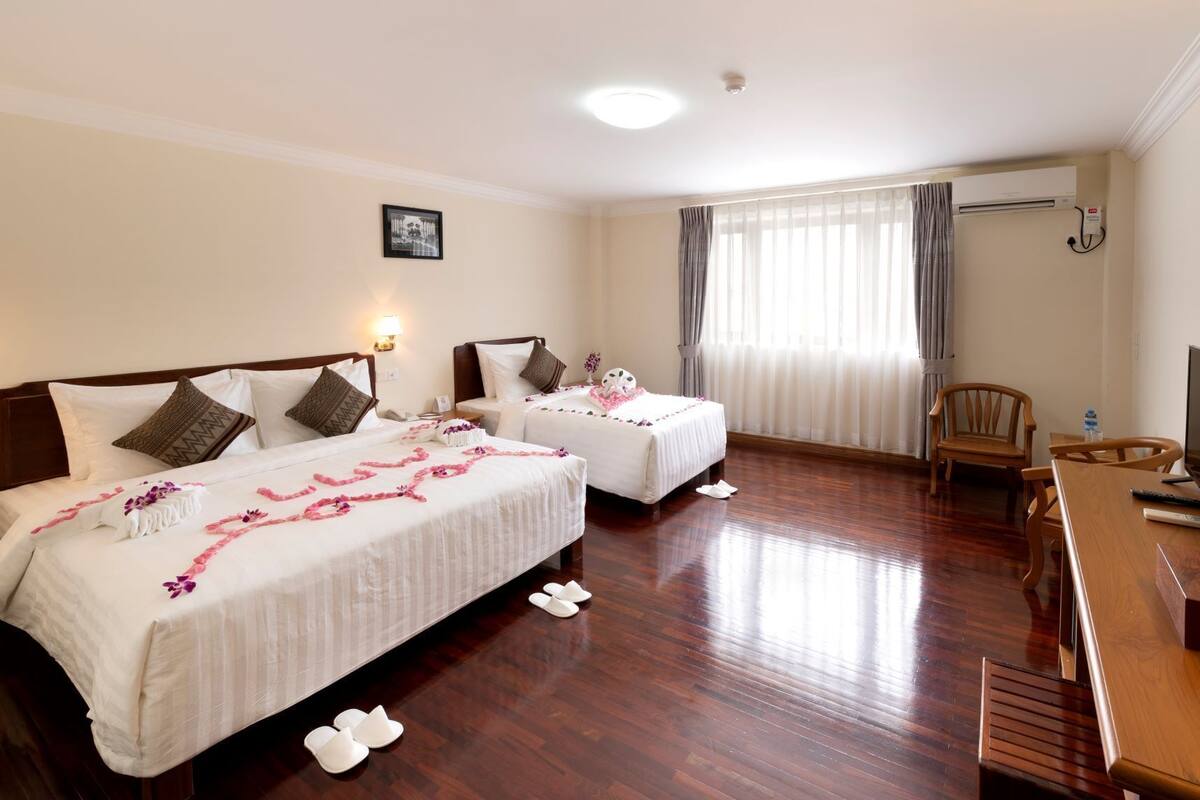 Quarto de hotel com duas camas, uma escrivaninha, uma cadeira e uma televisão.