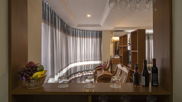 A dining area with a table set for two, a fruit basket, wine bottles, and a bar area with glasses. - Lin Unity Win Hotel (Yangon)
