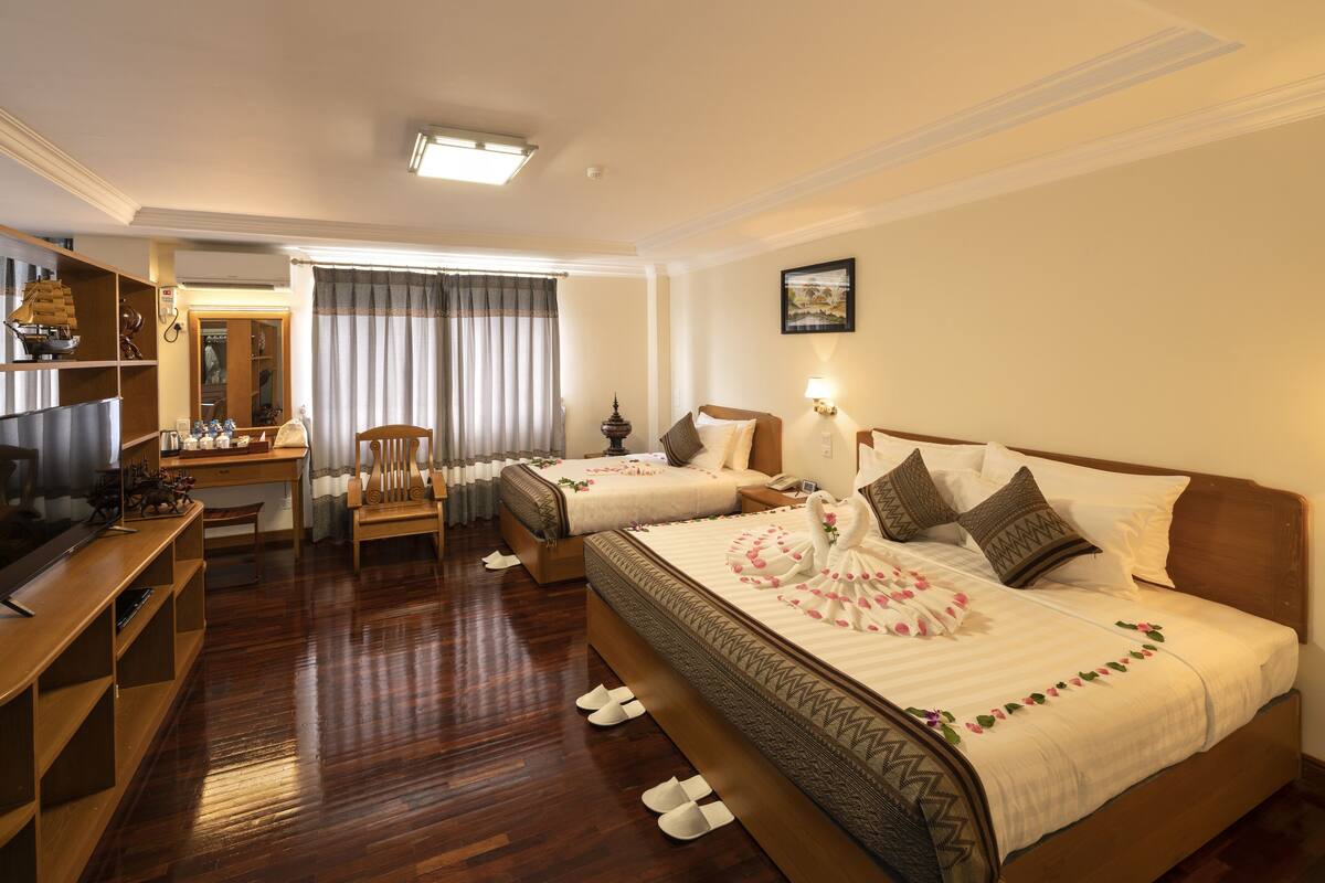 Quarto de hotel com duas camas, uma escrivaninha, uma cadeira, uma televisão e um guarda-roupa.