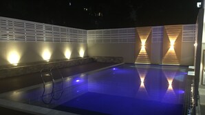 A swimming pool with a blue-lit water feature, surrounded by a white wall with built-in lighting. - Lin Unity Win Hotel (Yangon)