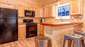 Une cuisine rustique aménagée dans une cabane en bois, comprenant un réfrigérateur, une cuisinière, un four à micro-ondes et des placards en bois.