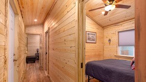 Une cabane en bois avec un lit simple, un ventilateur de plafond et un tableau encadré au mur.