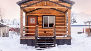 Une cabane en bois avec une porte d’entrée, une fenêtre et un escalier menant à l’entrée.