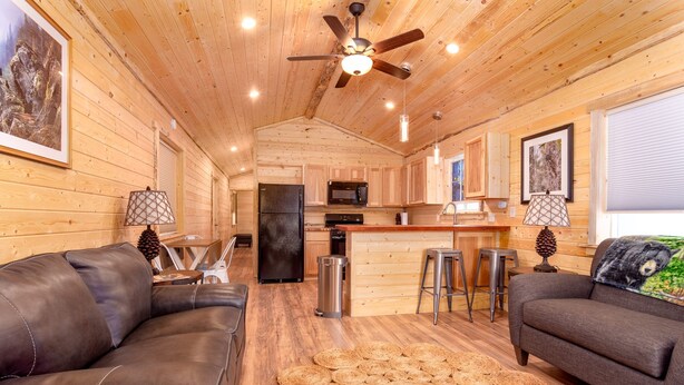 Un intérieur de chalet chaleureux avec une cuisine, deux canapés et un ventilateur de plafond.