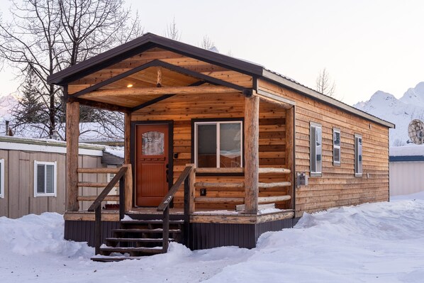 Une cabane en bois dotée d’une véranda, d’une porte d ’entrée et d’un escalier menant à l’entrée.