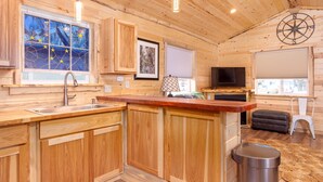 L’intérieur d’un chalet en bois comprend un coin cuisine, une table à manger, un téléviseur et un coin salon confortable.
