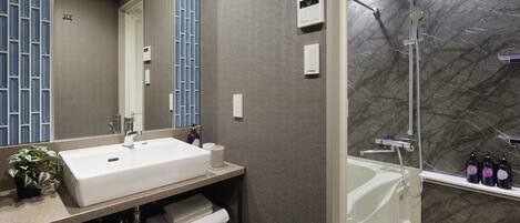 A modern bathroom with a large white sink, a mirror, a shower with a glass door, and a marble wall.