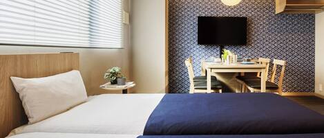 A hotel room with a bed, a desk, and a TV on the wall.