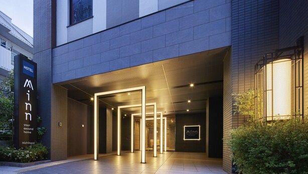 L'ingresso di un hotel dal design moderno, con un'imponente insegna 'Minn' e un percorso illuminato che conduce all'interno.