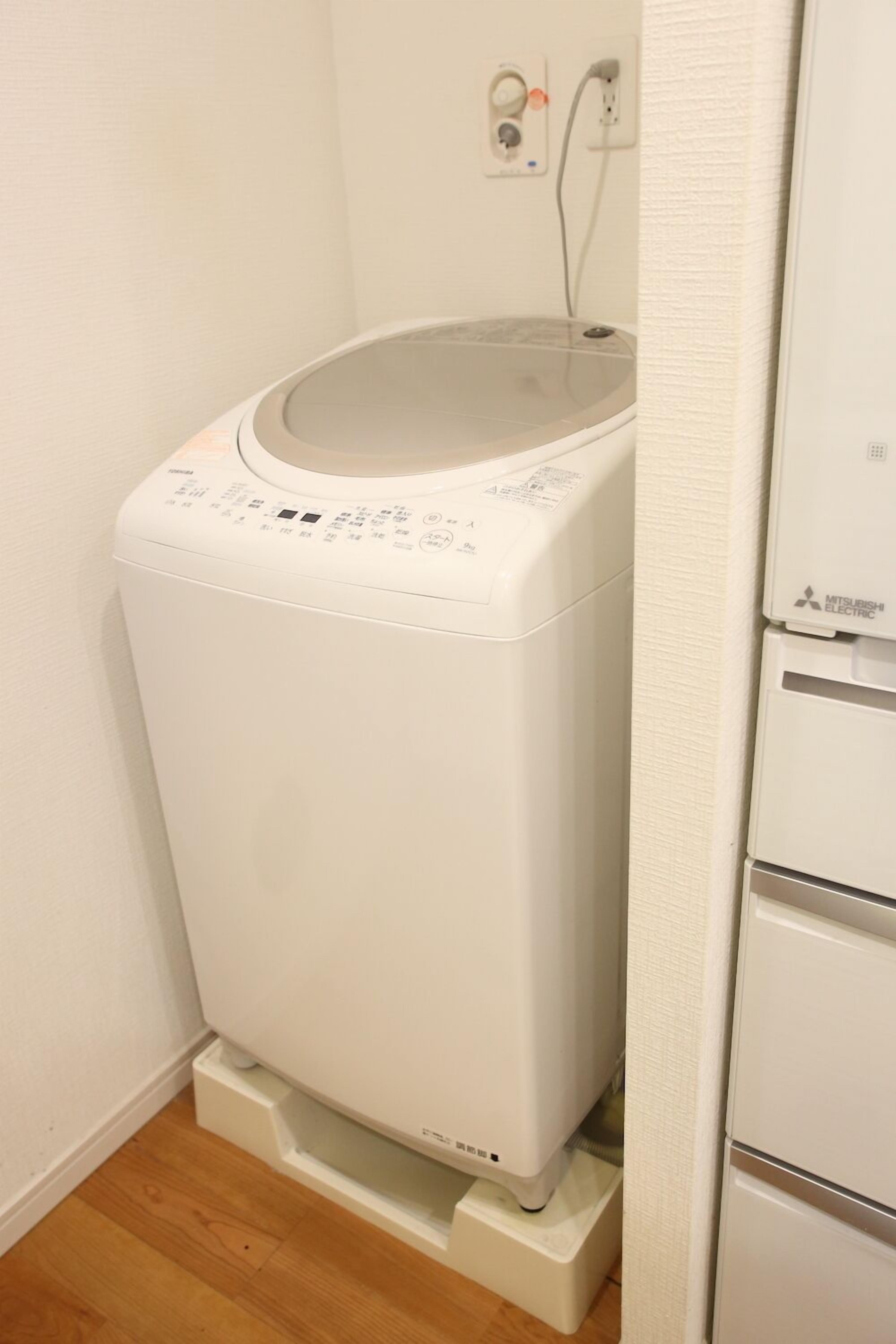 A white washing machine in a corner of a room with a wooden floor.