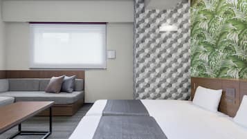 Una habitación de hotel moderna con un sofá, una cama, una mesita, una ventana con persianas, un papel tapiz con diseño geométrico y un papel pintado con hojas verdes.