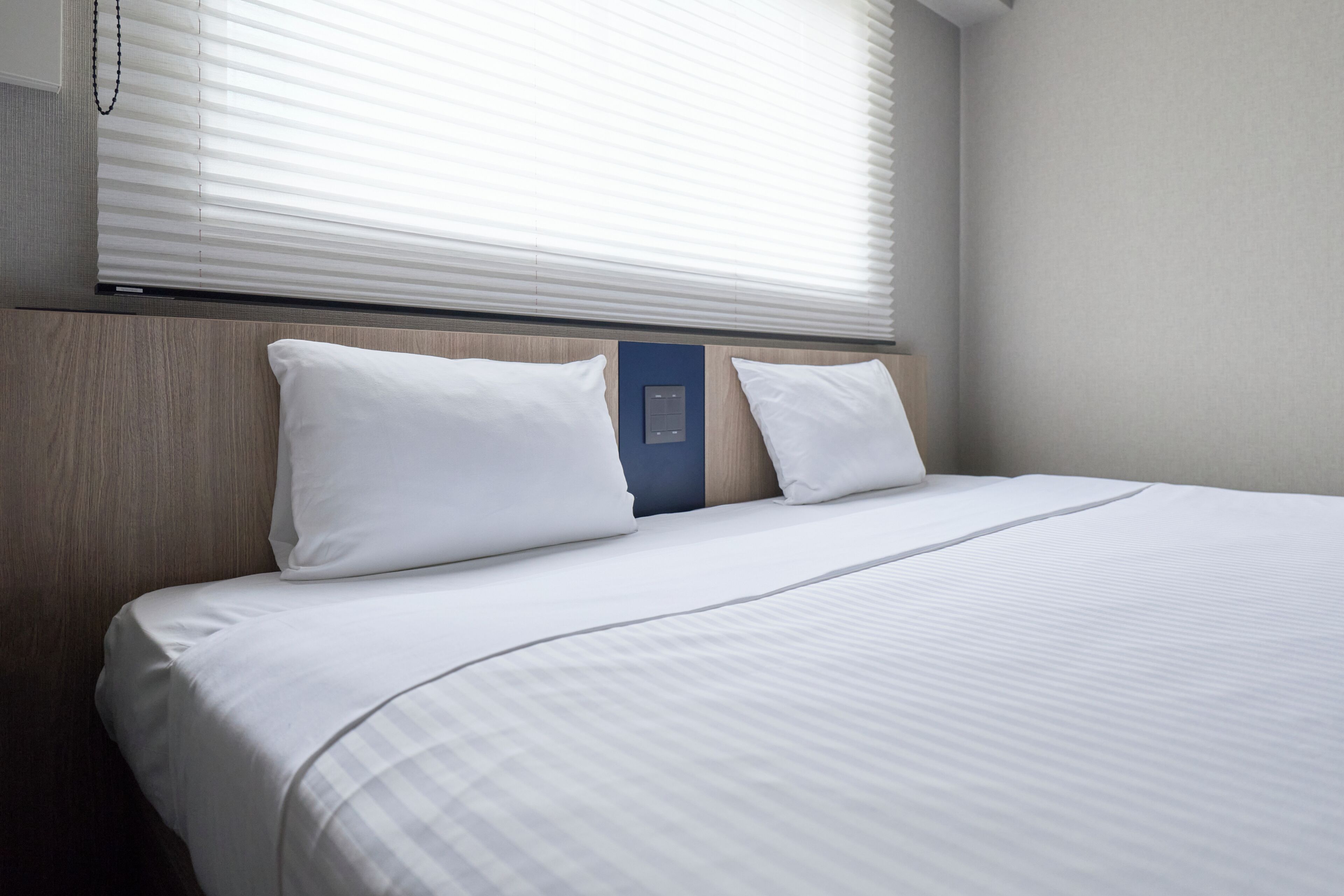 A neatly made bed with white bedding, a wooden headboard, and a blue panel on the wall.
