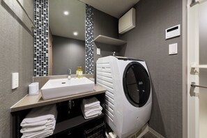 A modern bathroom with a sink, mirror, and a built-in washing machine. - MONday Apart Hamamatsucho Daimon (Tokyo)