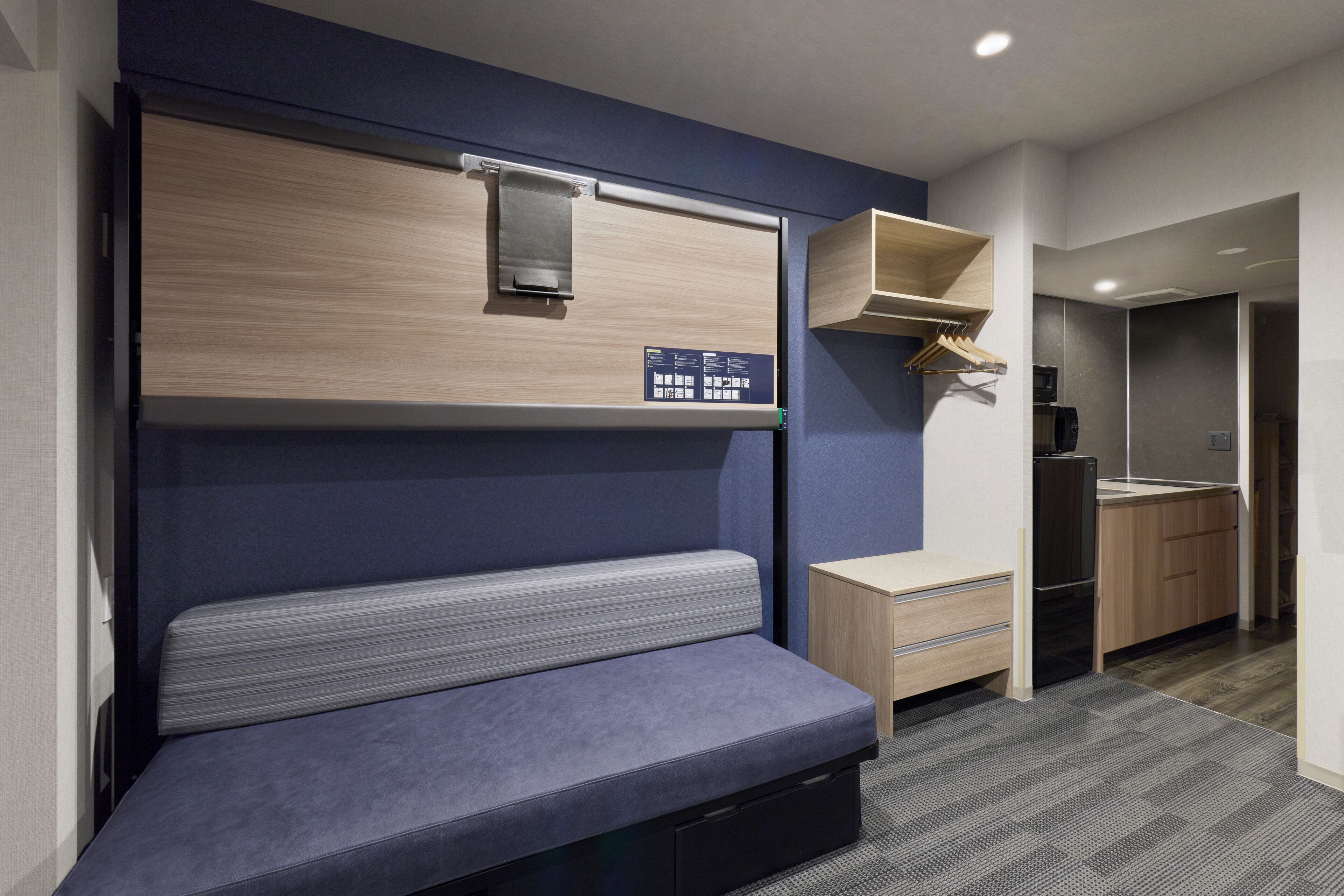 Ein kleines Zimmer mit Etagenbett, Schreibtisch, Kleiderschrank und einer Mikrowelle.