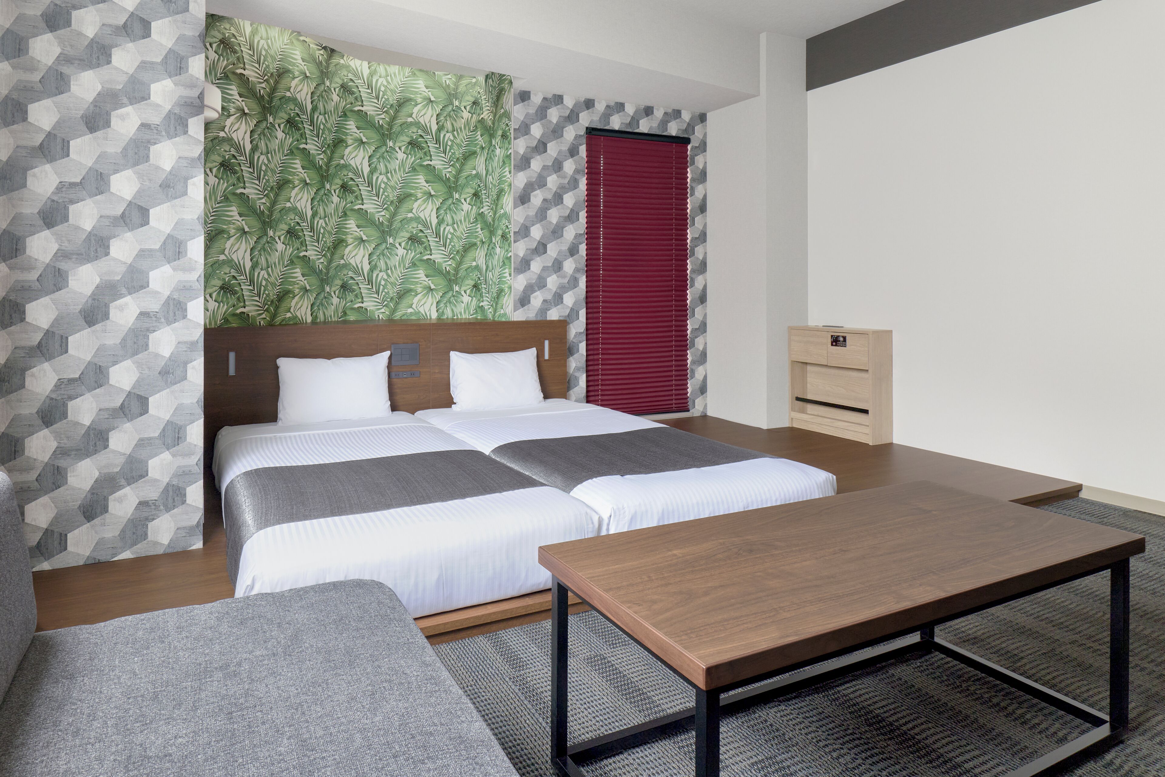 A hotel room with two beds, a wooden table, a desk, and a patterned wall.