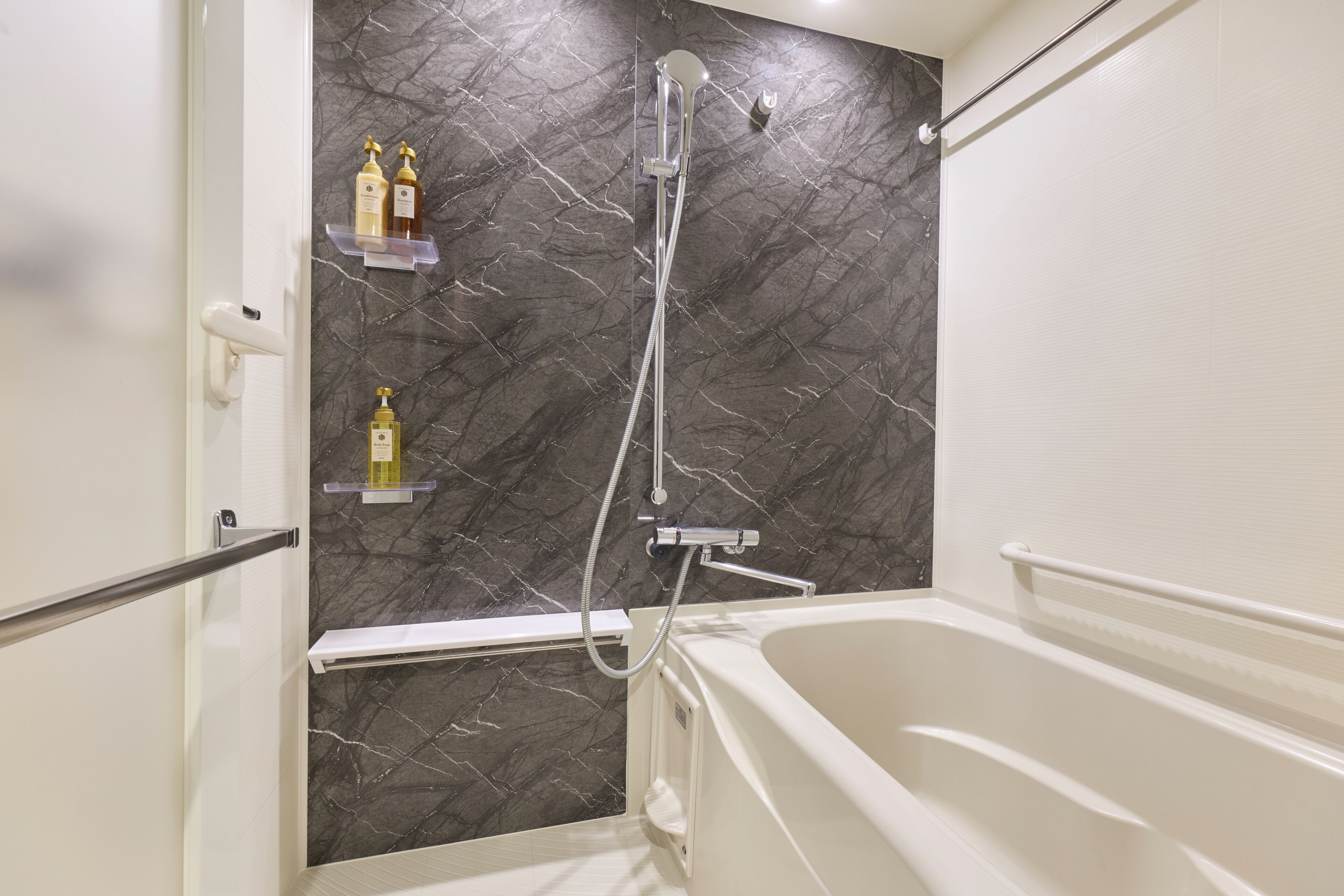 Une salle de bain avec un mur en marbre, une baignoire et deux étagères contenant des articles de toilette.