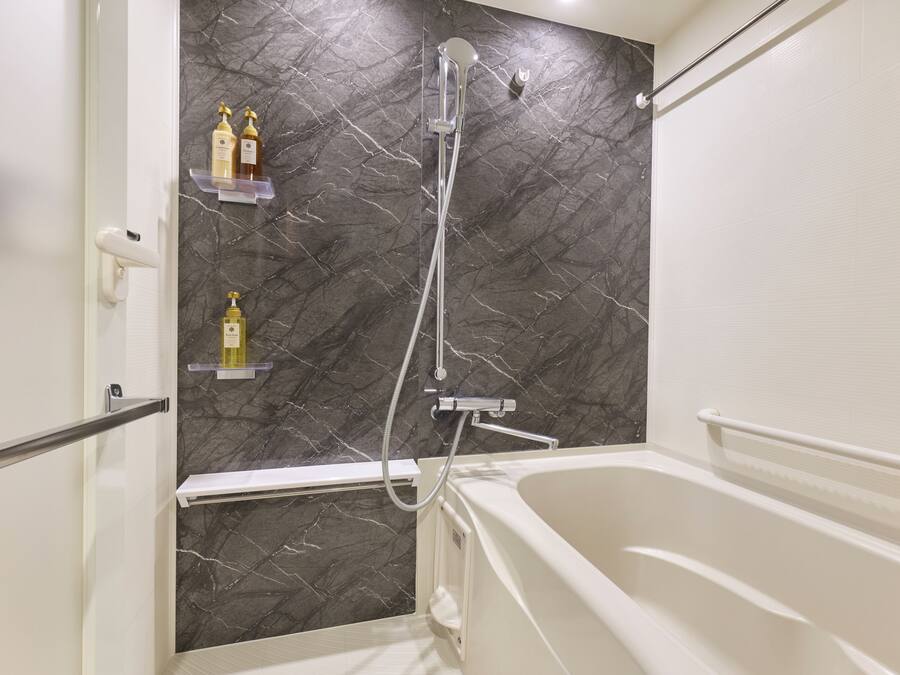 Une salle de bain avec un mur en marbre, une baignoire et deux étagères contenant des articles de toilette.