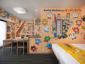 Ett hotellrum med en säng, ett skrivbord och en stol. Väggarna är dekorerade med tecknade figurer och orden ”Hotel Monday”.