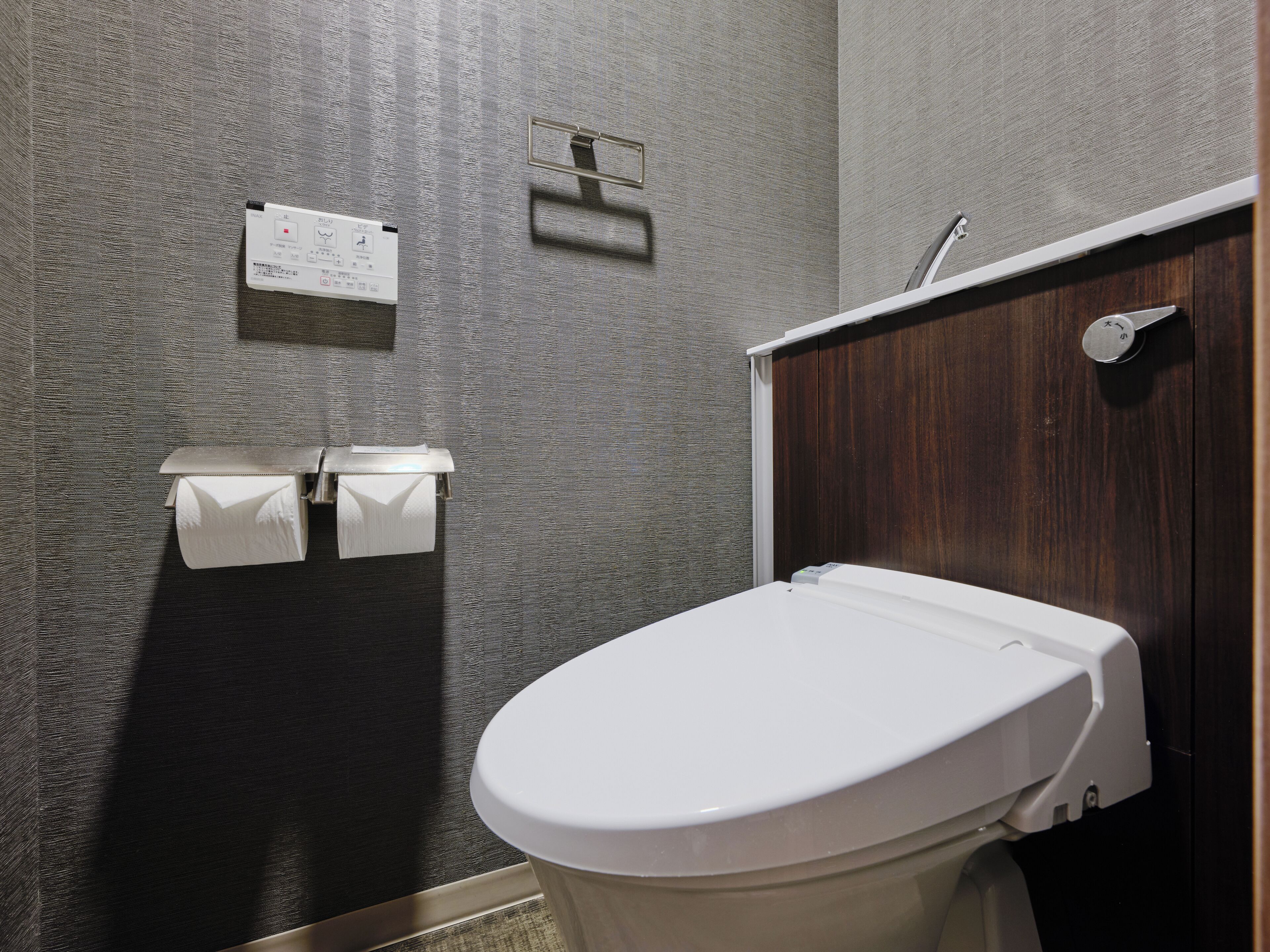 A bathroom with a toilet, paper towel dispenser, and a wooden door.