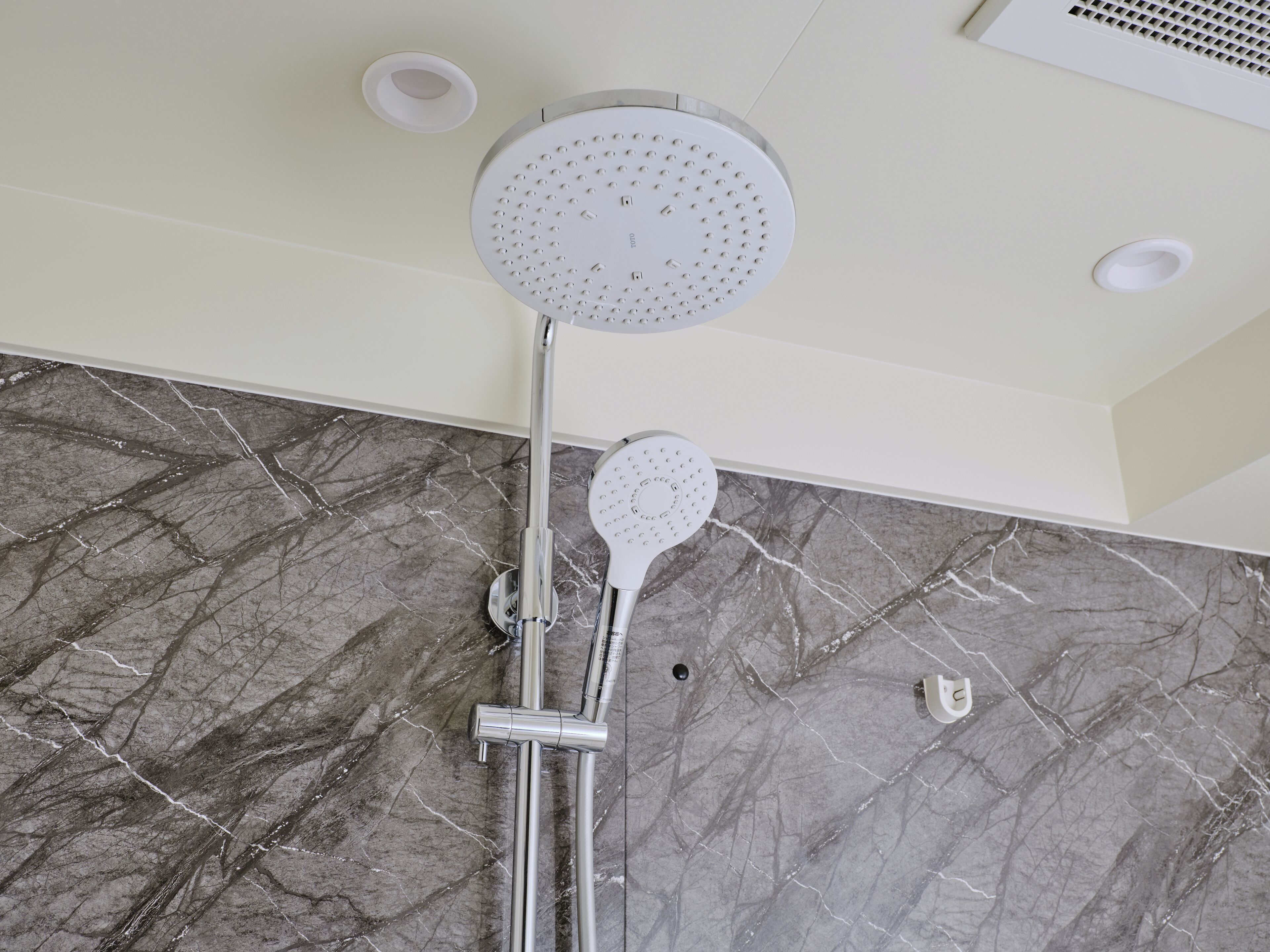 A shower with a round head and a handheld attachment, mounted on a wall with a marble pattern.