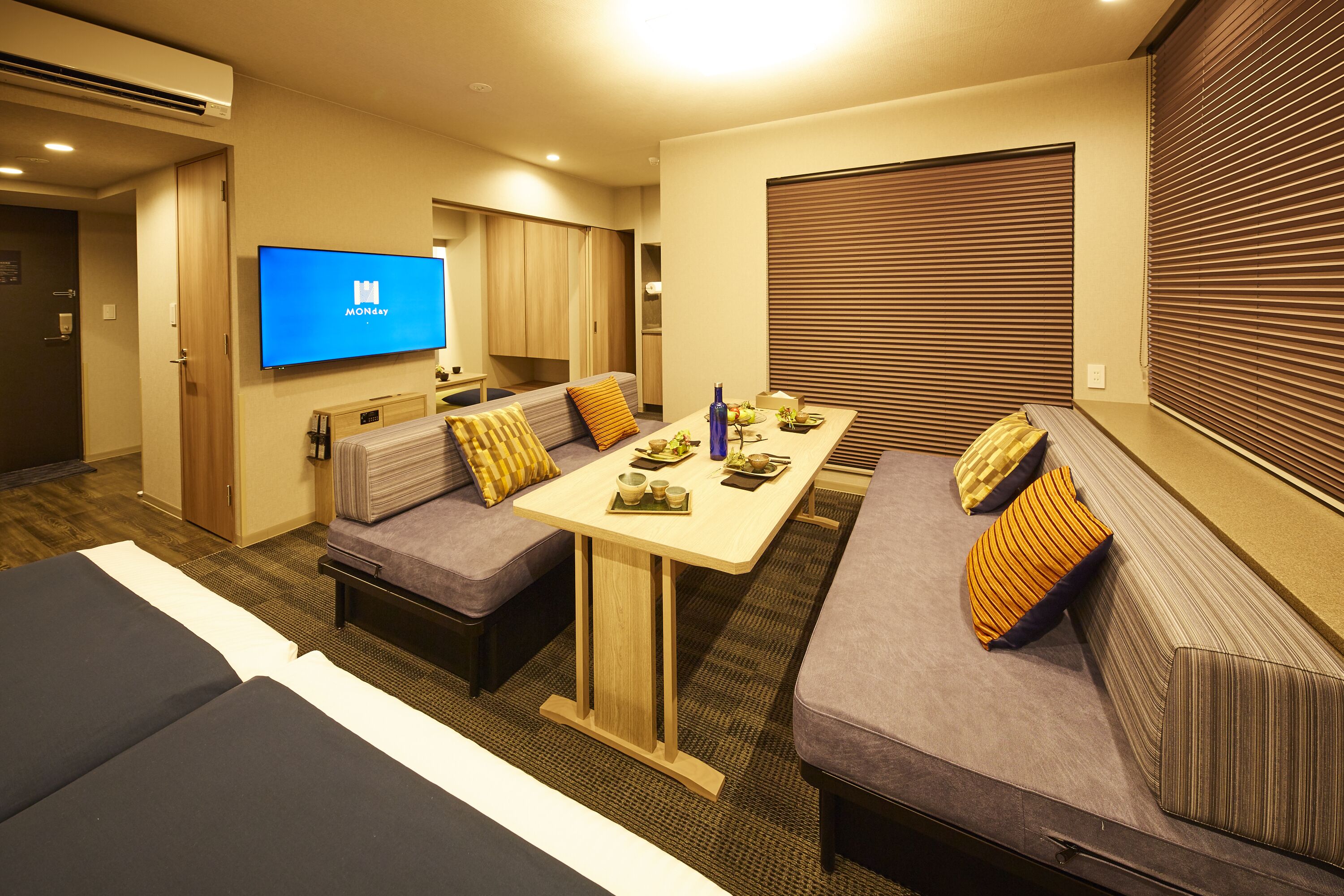 A hotel room with a sofa set, a dining table, and a TV mounted on the wall.