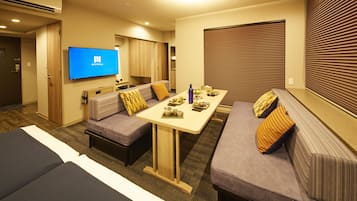 A hotel room with a sofa set, a dining table, and a TV mounted on the wall.