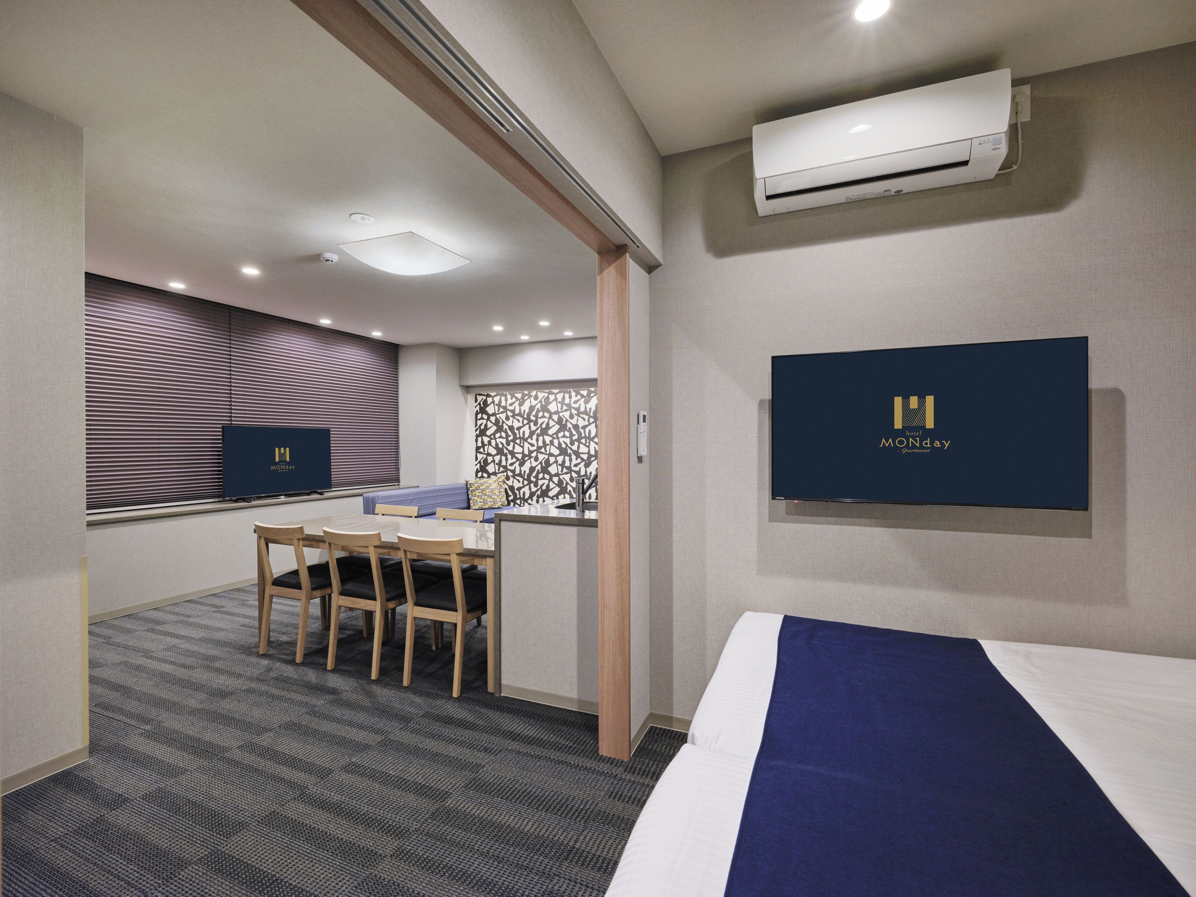 A hotel room with a bed, a desk with a chair, a television, and an air conditioning unit.