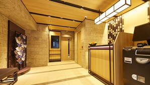 A hotel lobby with a wooden reception desk, a vending machine, and a wall with a decorative fan arrangement. - MONday Apart Premium Hamamatsucho (Tokyo)