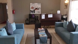 Una sala de estar moderna con dos sofás azules, una mesa de centro y un mostrador de recepción con un cartel que indica acceso a WiFi.