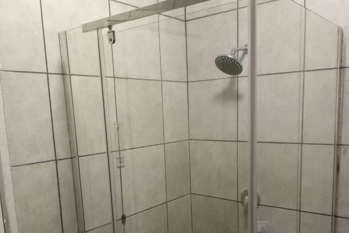 Une cabine de douche fermée par des parois en verre, dotée d’un carrelage à motifs géométriques, d’un pommeau de douche à main et d’une étagère en métal.