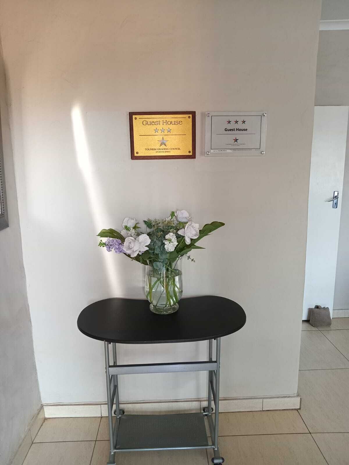 A reception area with a black table and a vase of flowers, a plaque indicating 'Guest House' and 'Tourism Grading Council of South Africa', and a sign with three stars.