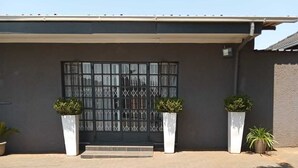 Un edificio con una entrada moderna, un camino de entrada pavimentado y dos macetas grandes con follaje.