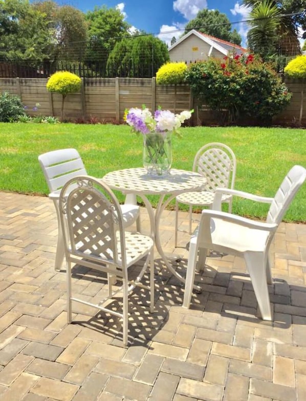 Une terrasse avec une table ronde et quatre chaises, entourée d’un sol en briques et d’une clôture en bois.
