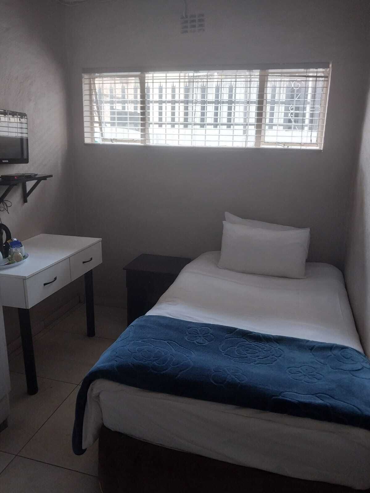 Une pièce comprenant un lit, un bureau, une chaise et une fenêtre avec des stores.