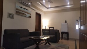 A living room with a sofa, two armchairs, a coffee table, a lamp, a whiteboard, and a refrigerator.