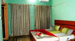 A room with a bed, a window with curtains, and a wall-mounted air conditioner.