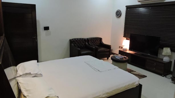 A bedroom with a bed, a dark leather armchair, a TV, and a small table with a lamp.