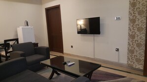 A living room with a sofa, a coffee table, a flat-screen TV mounted on the wall, a door, and a patterned wallpaper.