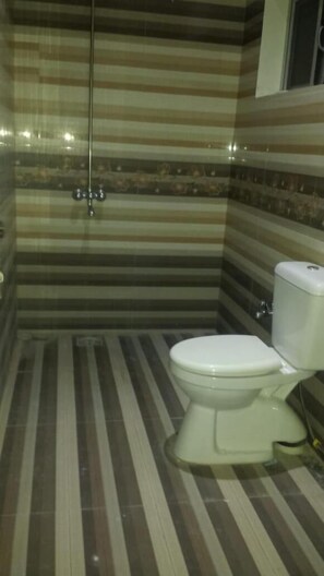 A bathroom with striped tile walls, a shower, and a toilet.
