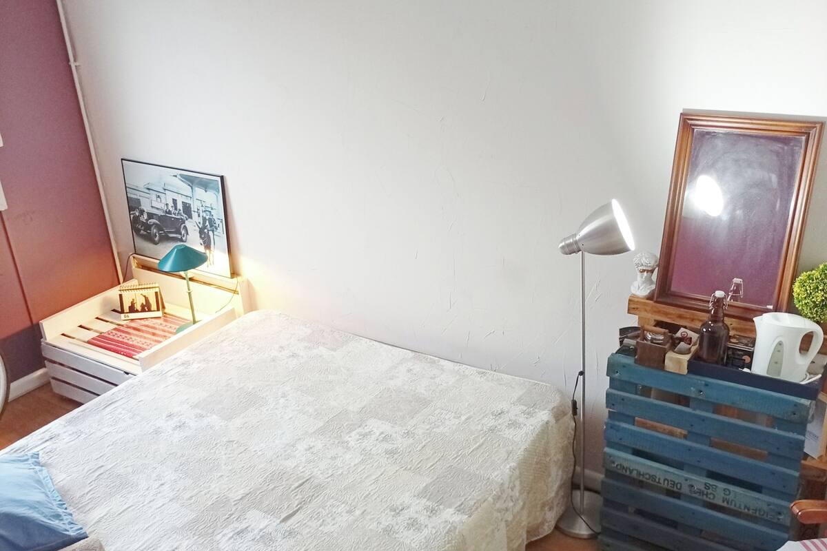 A bedroom with a bed, bedside table, lamp, picture frame, and a small plant.