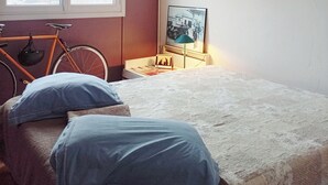 A bedroom with a bed, pillows, a bicycle, a window, and a wall-mounted lamp. - Longjumeau Chambres d'Hôtes - Book A Rest Paris (Longjumeau)