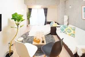 A modern hotel room with a bed, two sofas, a coffee table, a plant, and a TV.