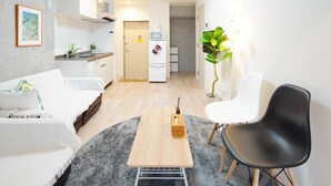 A modern living room with a sofa, a coffee table, and a black chair. There is a kitchen area with a microwave and a refrigerator in the background. - Asakusa Hotel 201 (Tokyo)