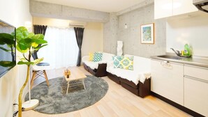 A compact living space with a sofa, a small dining table, a kitchen area, and a large potted plant. - Asakusa Hotel 201 (Tokyo)