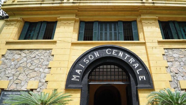 A building with a sign reading "MAISON CENTRAL" and a banner stating "3 minutes walk to HOA LO PRISON".