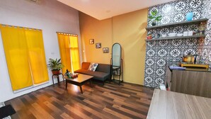 A living room with a sofa, coffee table, and a mirror. There is a patterned wall and a shelf with decorative items.
