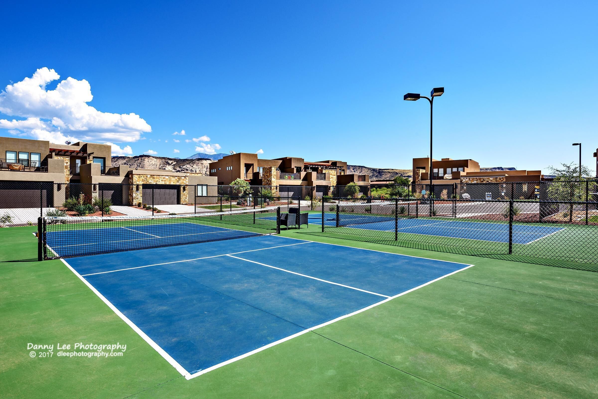 Een tennisbaan buiten met een net, omringd door gebouwen en een heldere lucht.