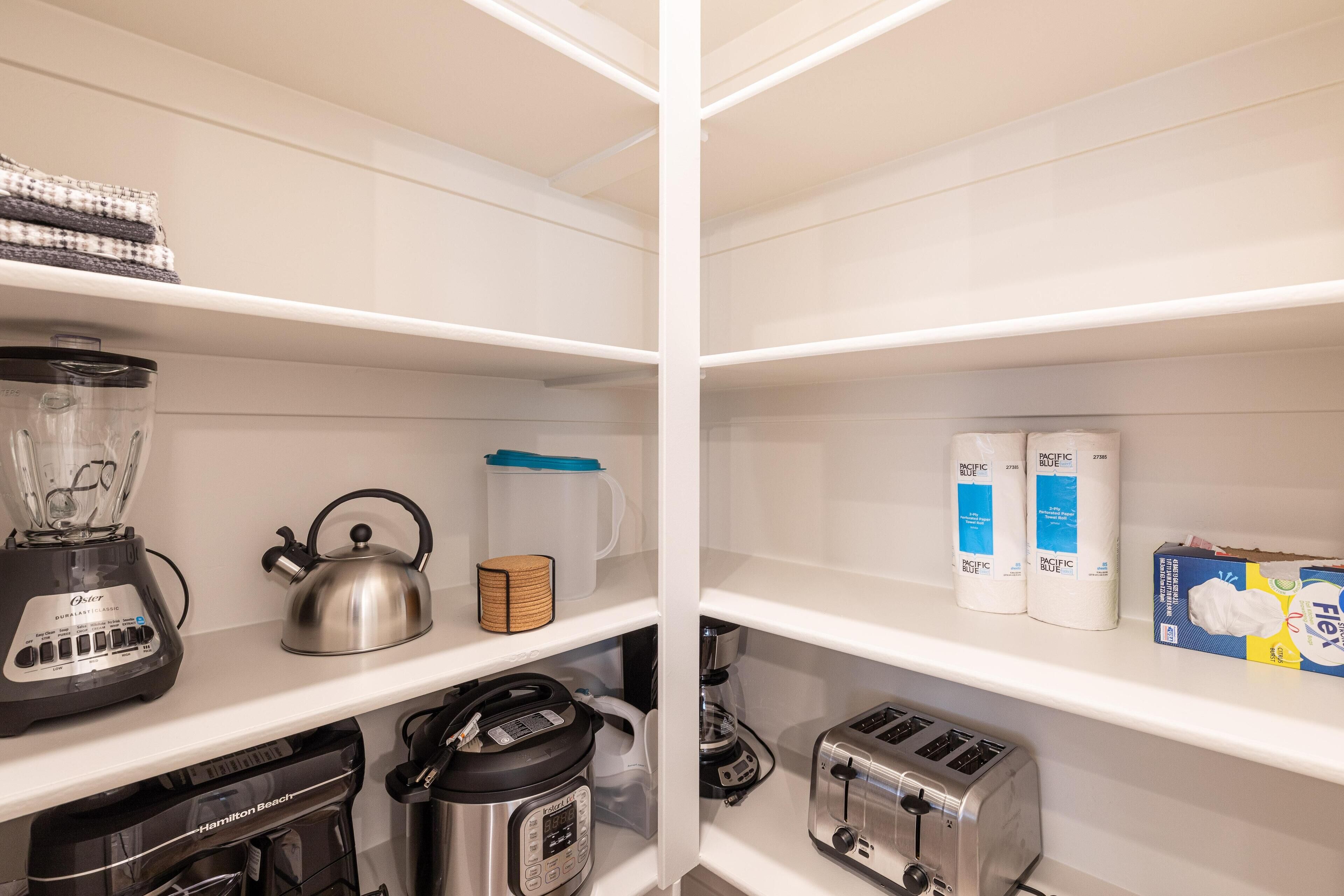 A kitchen with a blender, kettle, toaster, and a coffee maker on the shelves.