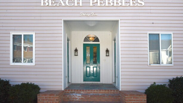Un edificio con un letrero que dice "BEACH PEBBLES Thirty Two" y una puerta verde con dos ventanas a cada lado.